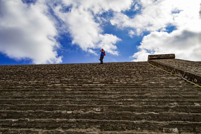 Low angle view of man standing on staircase against cloudy sky