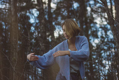 Young woman with short hair dancing against trees in forest