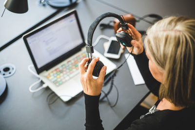 High angle view of businesswoman using headphones attached to laptop at desk in office