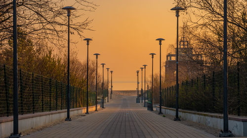 Footpath by street against sky during sunset