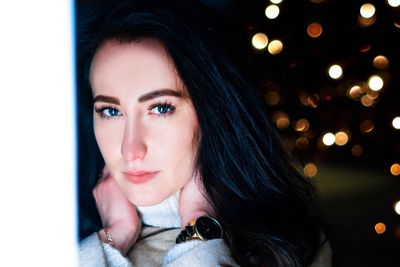 Close-up portrait of beautiful woman against illuminated lights