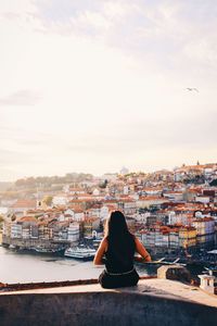 Rear view of woman sitting on retaining wall against sky