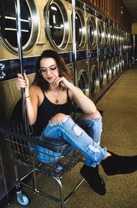 Young woman sitting in basket at laundromat