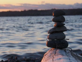 Stack of pebbles on shore against sky during sunset