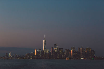 Sea and buildings against sky in city at dusk