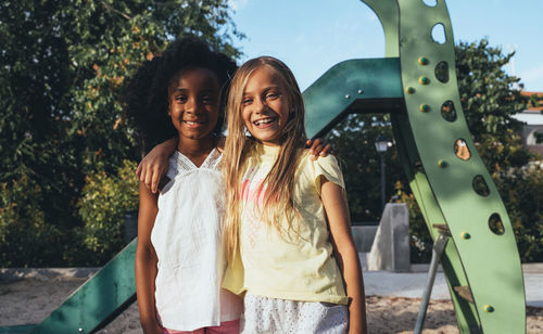 Friendly active diverse girls standing and looking at camera having fun at slide in bright day