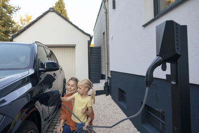 Mother guiding daughter to charge electric car in front yard