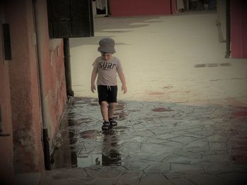 Rear view of girl walking on wet street in city