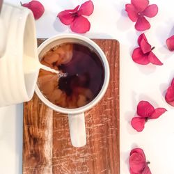 High angle view of milk pouring from container in tea cup on cutting board