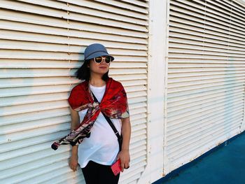 Woman wearing sunglasses looking away while standing against wall