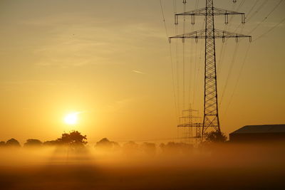 Silhouette electricity pylon on field against sky during sunset