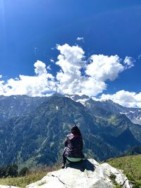 Rear view of man sitting on mountain against sky