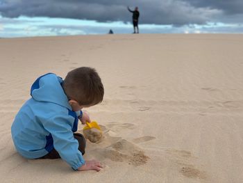 Rear view of boy playing with sands at beach 