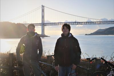 Men with bicycles standing in front of suspension bridge against sky