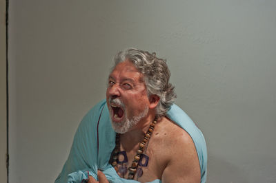 Portrait of shirtless man with arms raised against wall