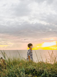 Boy standing on field against sky during sunset