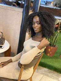 Portrait of smiling young woman with curly hair sitting on chair