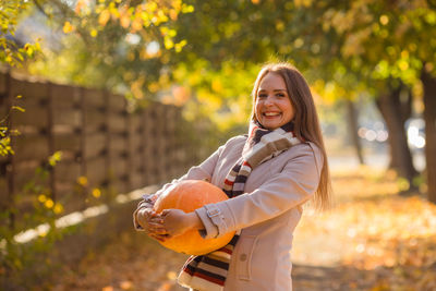 Portrait of young woman with arms raised standing against trees