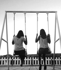 Rear view of women swinging against clear sky at playground