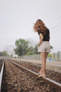 Woman walking on railroad track against sky