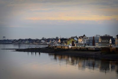 River by houses and buildings against sky at sunset