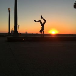 Silhouette of a person doing handstand against the sky at sunset