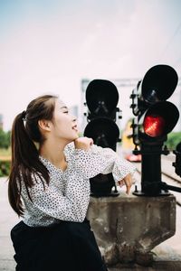 Side view of young woman looking away while crouching by traffic signal against sky