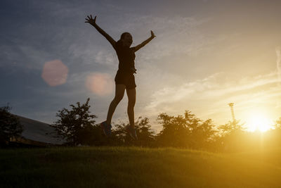 Woman jumping over field against sky
