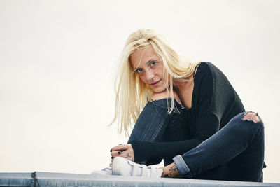 Portrait of young woman sitting against wall