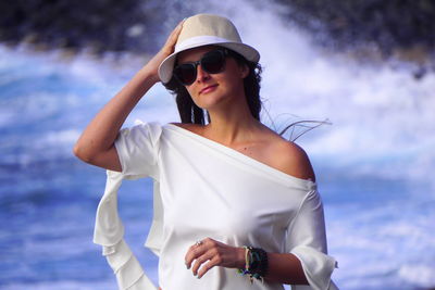 Young woman wearing sunglasses standing against sea