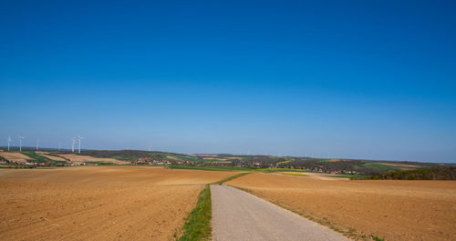 Road amidst field against clear blue sky