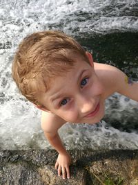 Directly above shot of shirtless boy smiling while standing in river