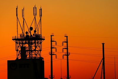Silhouette electricity tower against orange sky during sunset