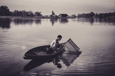 Man sitting in boat on lake against sky