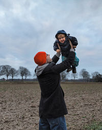 Playful father lifting daughter on field against sky