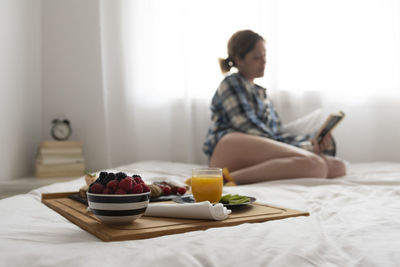 Focused breakfast tray and unfocused woman reading on background.