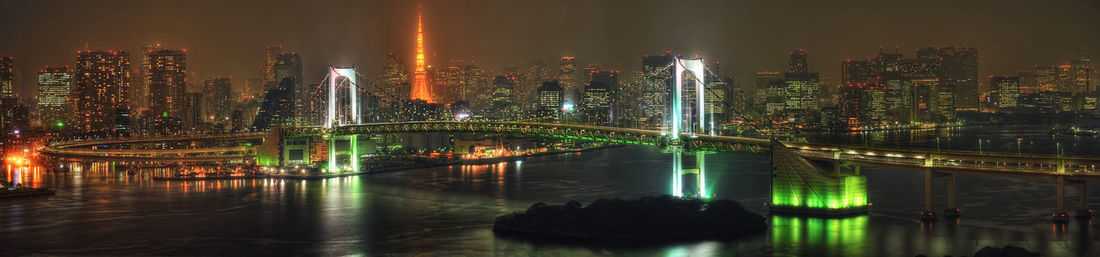 Illuminated bridge over river by buildings against sky at night