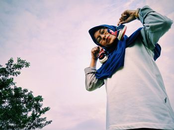 Low angle view portrait of woman holding small shoes standing against sky