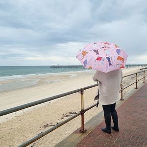 Rear view of woman with umbrella on beach against sky
