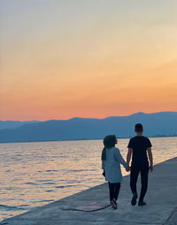 Rear view of couple on shore against sky during sunset