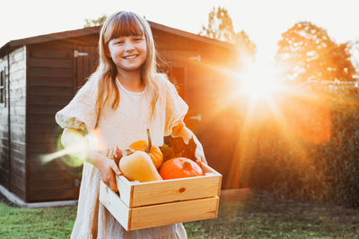 A girl in the evening sun stands in the backyard of a house with a box of pumpkins. harvesting. 