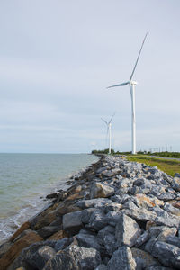 Wind turbines on rocks by sea against sky