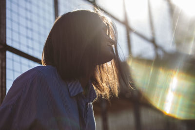 Close-up of young woman against glass window during sunny day