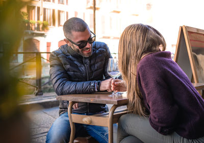 Couple holding wineglasses on table talking while sitting at outdoor cafe