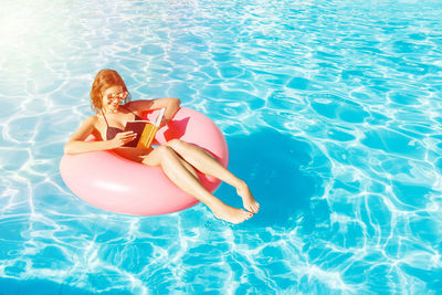 Smiling young woman enjoying in swimming pool with inflatable ring during summer