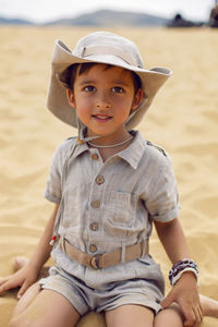 Portrait boy child traveler in a suit of an archaeologist and wearing hat sitting on sand in desert