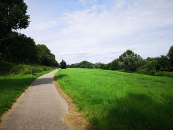 Empty road amidst field against sky