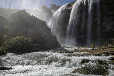 Man standing against scenic waterfall