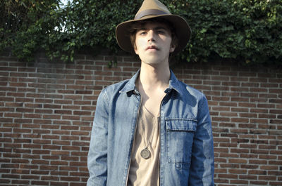 Young woman wearing hat standing against brick wall