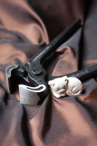 Close-up high angle view of cat figurine with work tool on brown textile